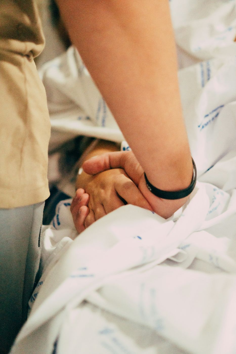 A woman sits beside her husband's hospital bed holding his hand, illustrating loss of consortium in South Carolina after a serious injury