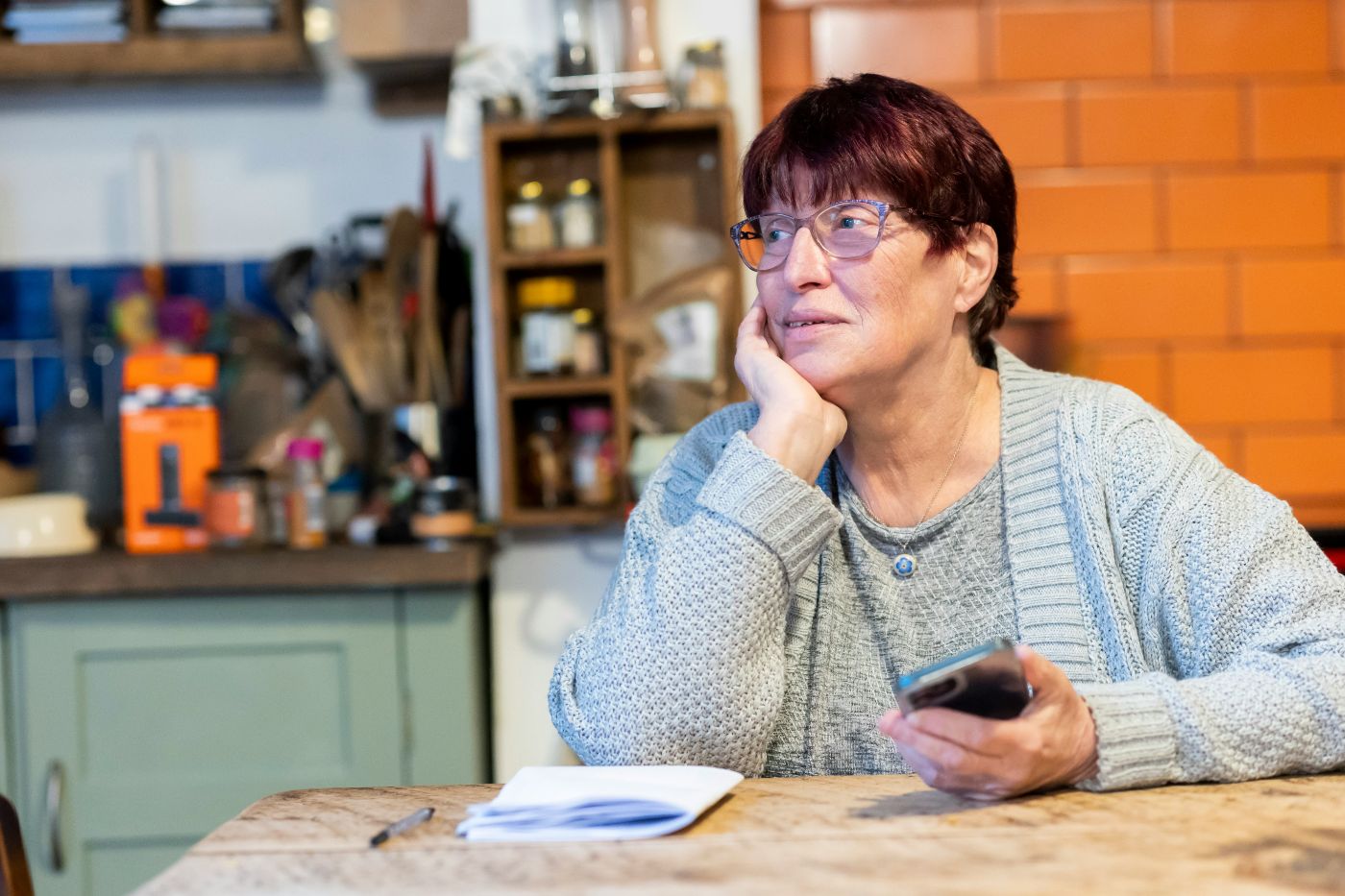 A woman in her sixties sits at her kitchen table with her phone, thinking through how to keep FEHB after divorce