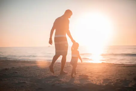 Holding child's hand at the beach during sunset