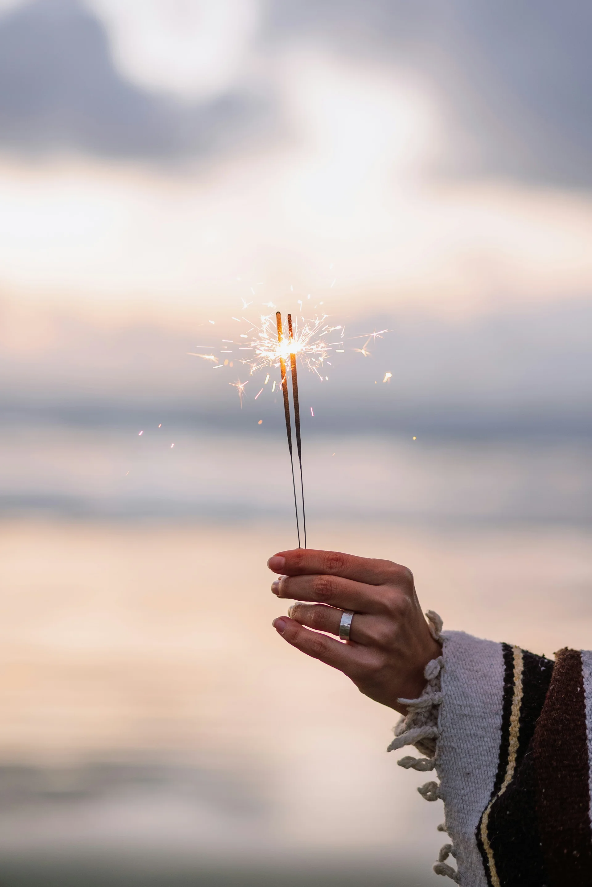 A hand holding two lit sparklers against an evening sky at the beach, illustrating a fireworks injury claim in South Carolina.
